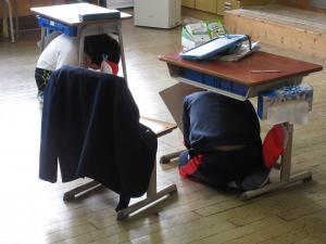 机の下に身をかがめる児童