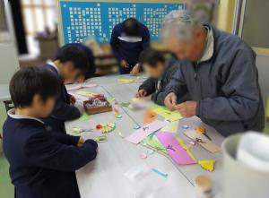 12月15日：地域の方が扇作りを教えてくださいました。テープ張りや紙折りなど細かい作業を根気強く行って、いくつも扇を完成させました。扇はしめ縄作りで使います。しめ縄作りは、12月23日でず。一緒にしめ縄を作りましょう。