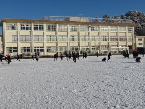 雪の積もったグラウンドで児童が遊んで